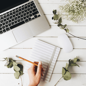 A computer and notepad with a virtual assistant ready to take notes.